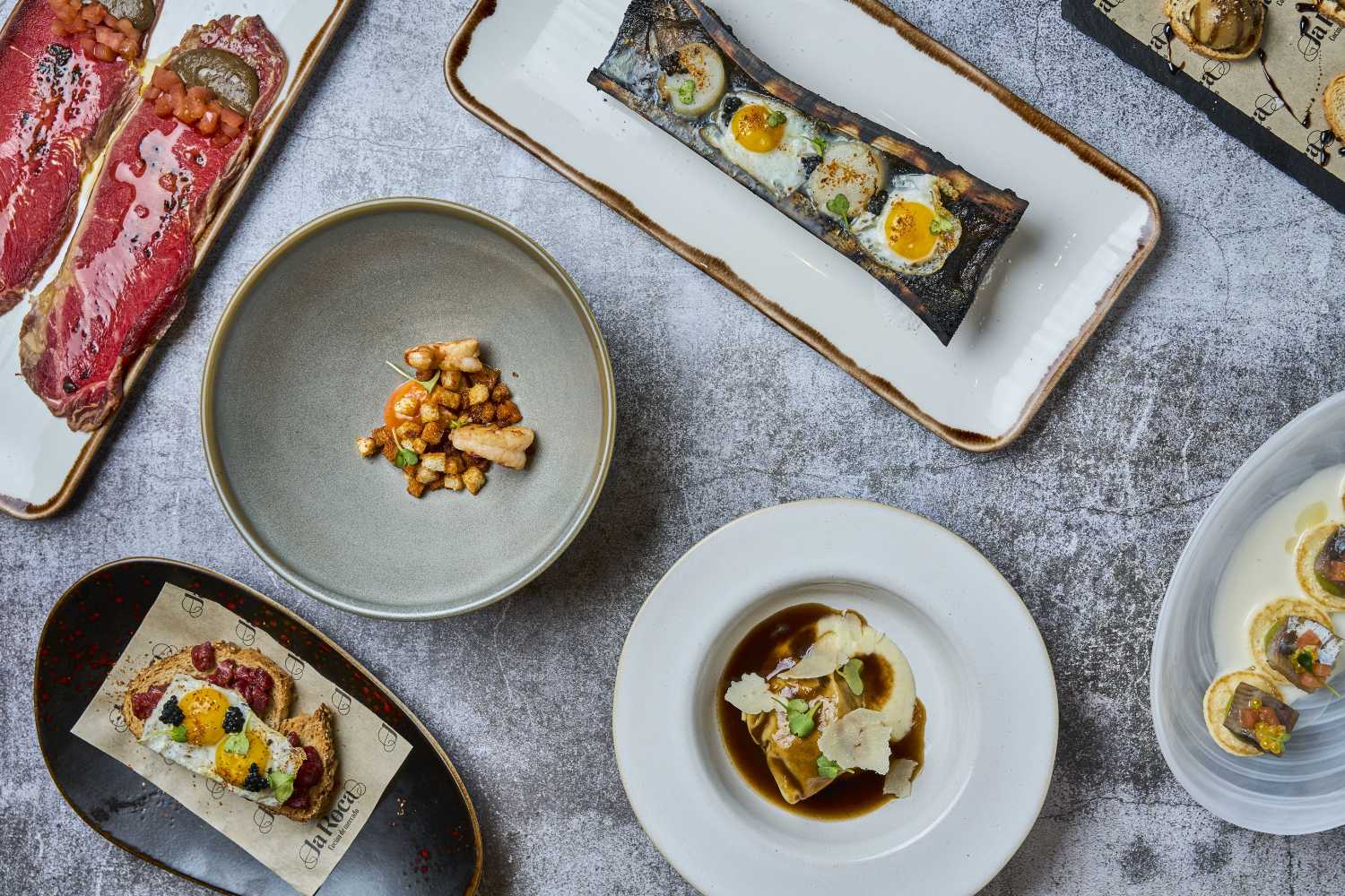 Vista cenital de varios platos de cocina de mercado en La Roca: tapas y platos gourmet.